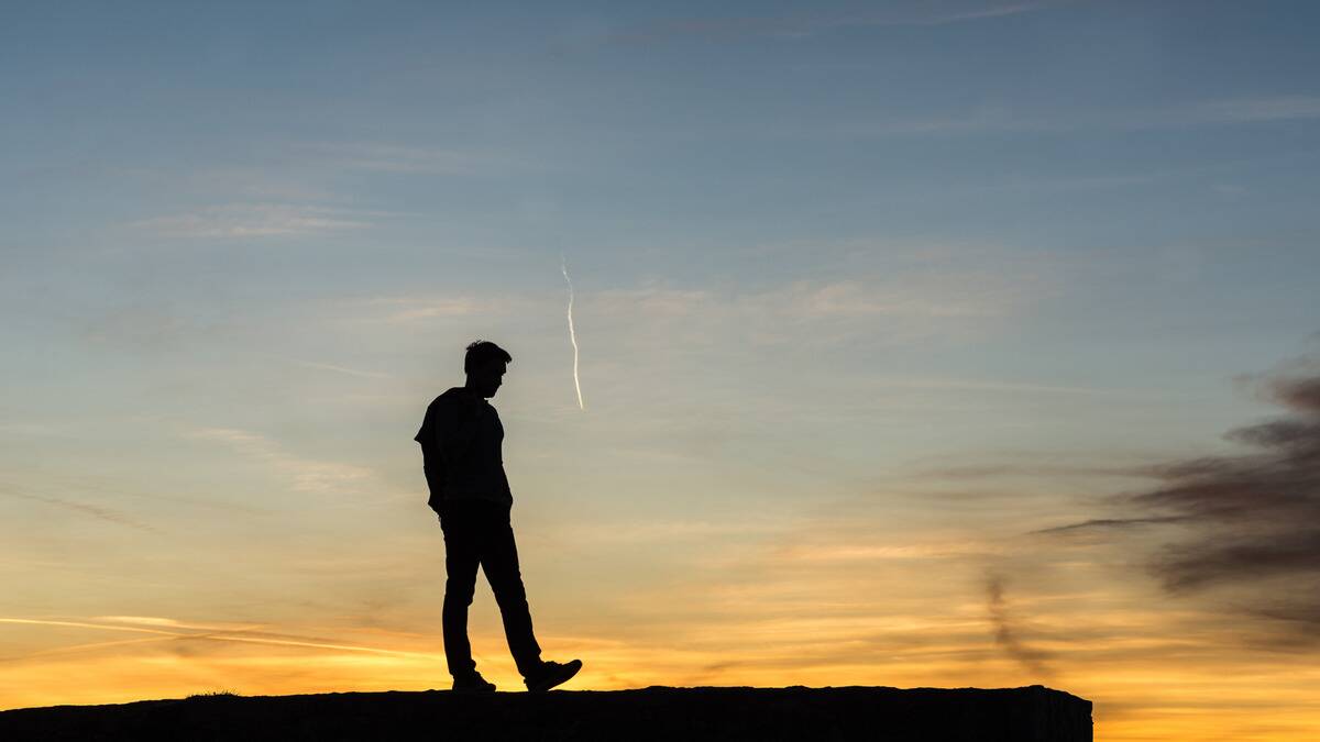 A silhouette of a man walking along the top of a wall, a sunrise sky behind him.