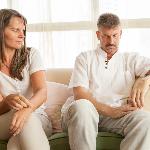 A couple sitting side by side on a couch but leaning away from each other, both looking at each other awkwardly.