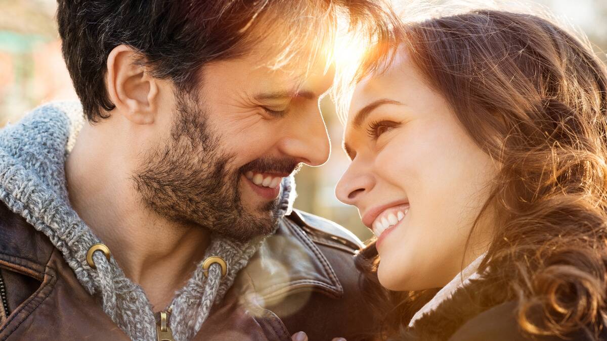 A close shot of a happy couple whose faces are close together, smiling at one another.