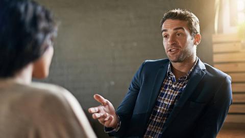 A man speaking confidently to someone who's mostly out of frame sitting across from him