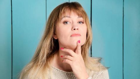 A close shot of a woman looking at the camera, one finger on her chin.