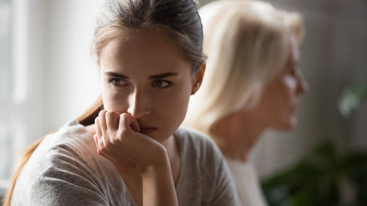 A close shot of a woman with her chin in her hand, looking annoyed or frustrated, a woman seen behind her, presumably her mother.