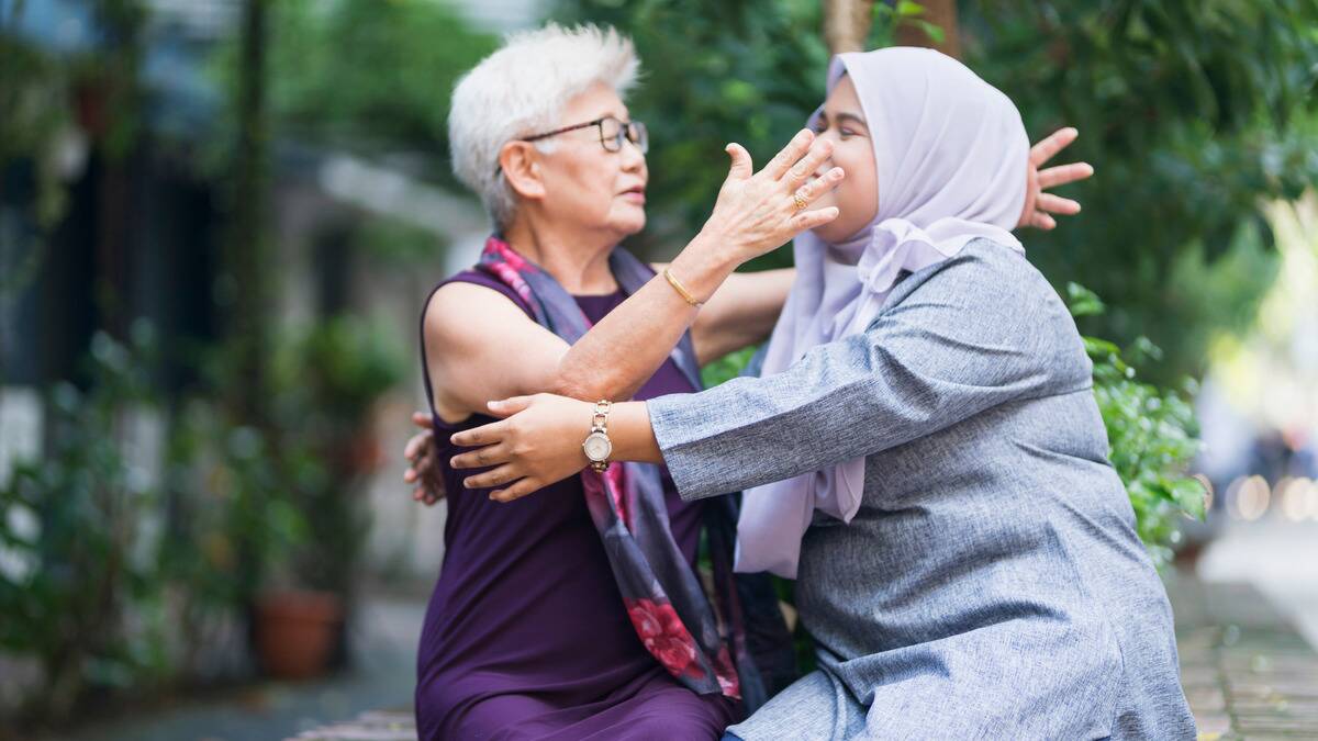 Two women sitting outside going in to hug each other.