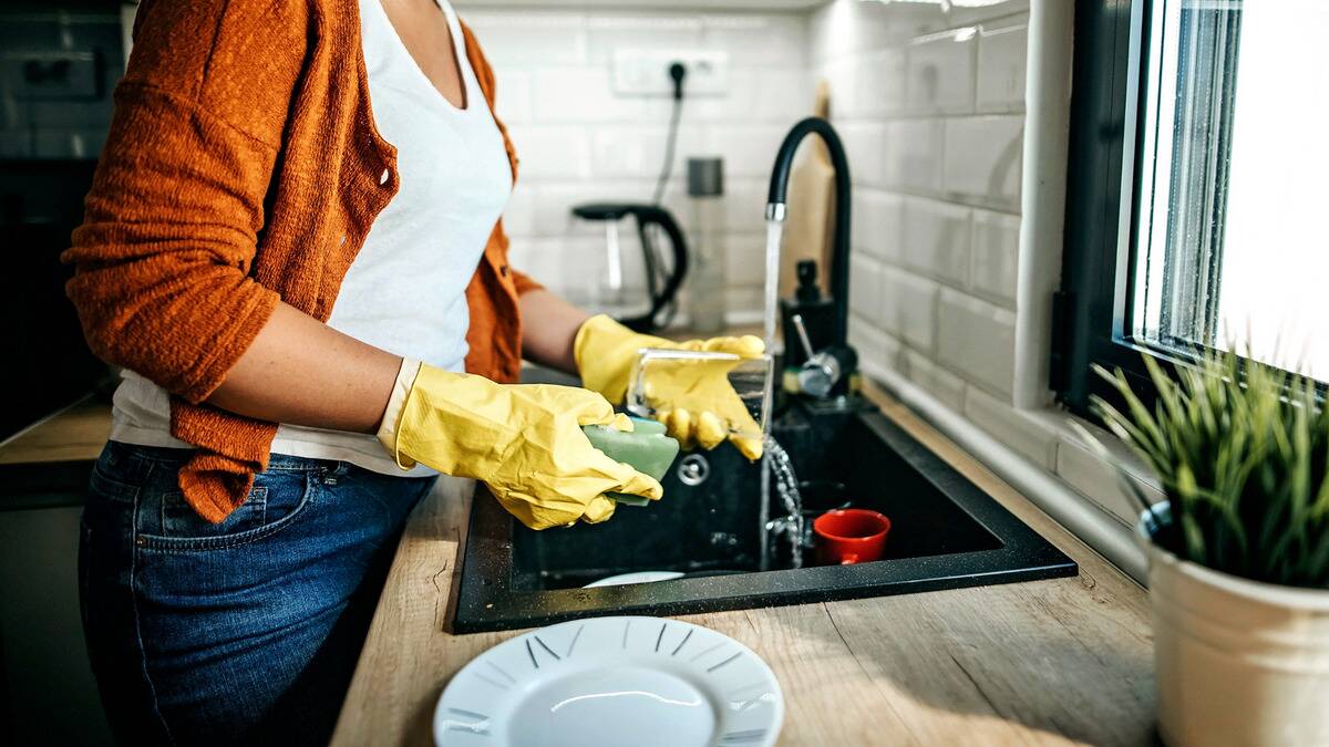 A woman in rubber gloves washing fishes in her sink.