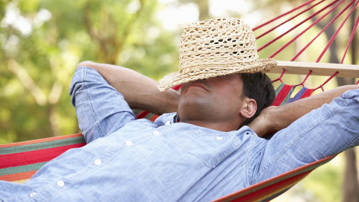 A close shot of a man lounging back in a hammock, a hat over his eyes.