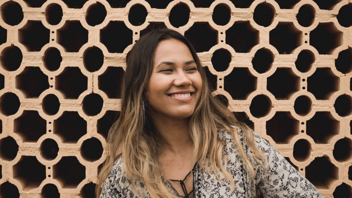 A woman smiling as she stands in front of a geometrically pattered wall outside.