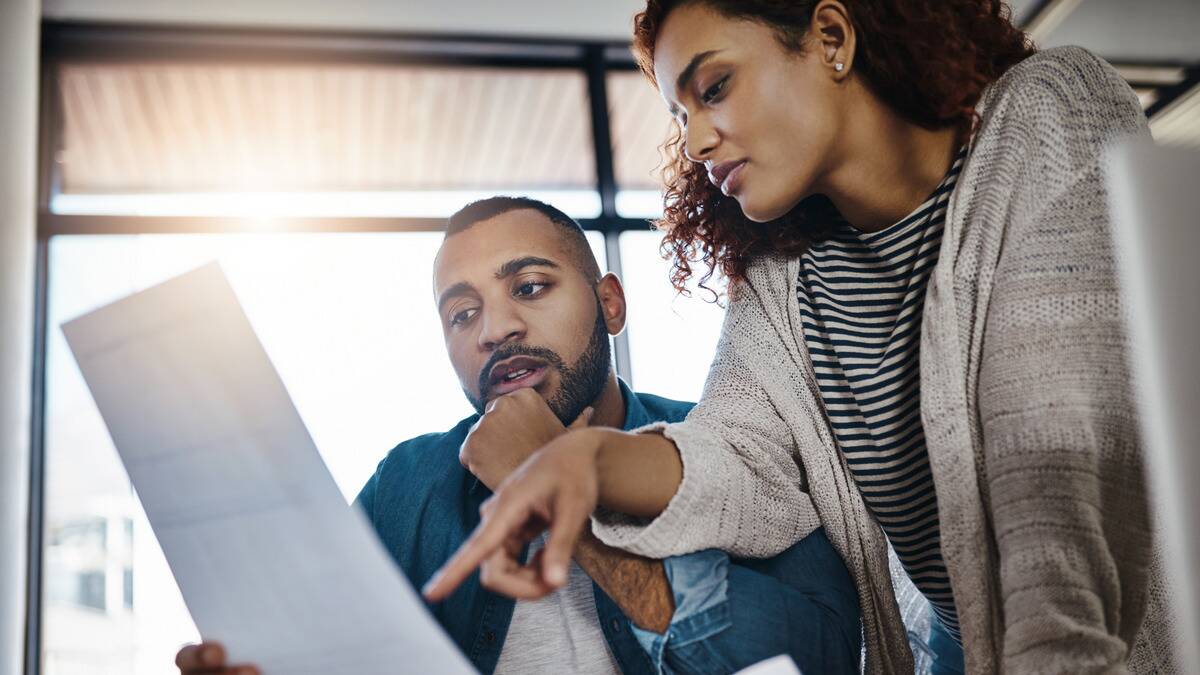 A man and a woman looking at a document together, the woman pointing something out while the man strokes his chin.