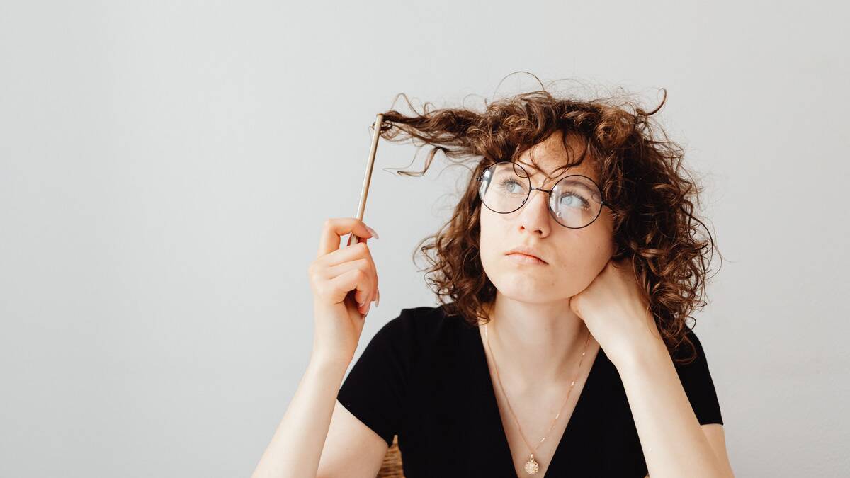 A woman resting her cheek on her hand, twirling her hair with a pencil as she thinks.