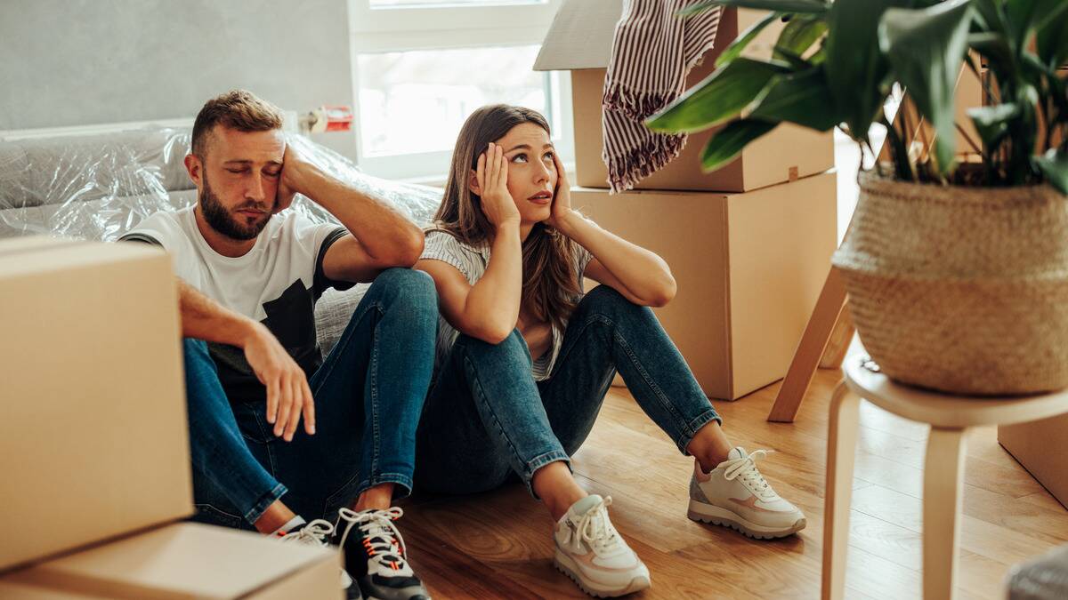 A couple sitting next to each other on the floor after just having moved somewhere, looking stressed while they're surrounded by boxes.