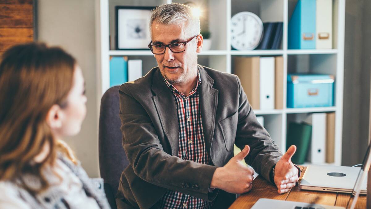 A man speaking to a woman he's mentoring at work, gesturing with his hands.