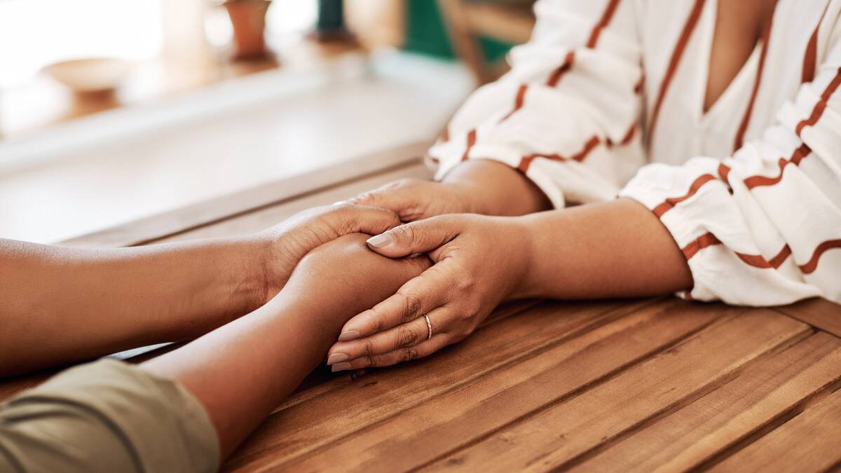 A close shot of two friends holding hands across a table.