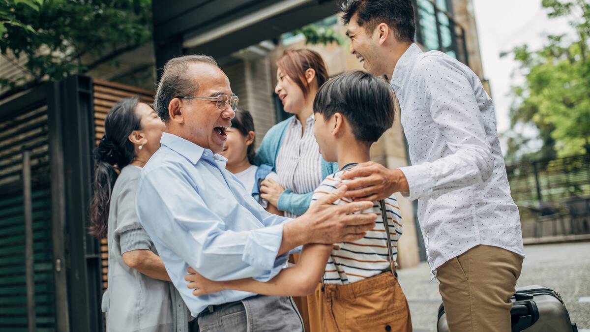 A family all greeting each other for a family reunion, the image focus on a man smiling as he goes to hug his grandson.