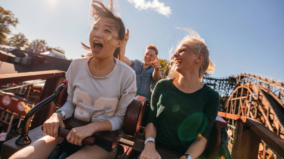 Three friends riding a roller coaster, all of them smiling while yelling in excitement.