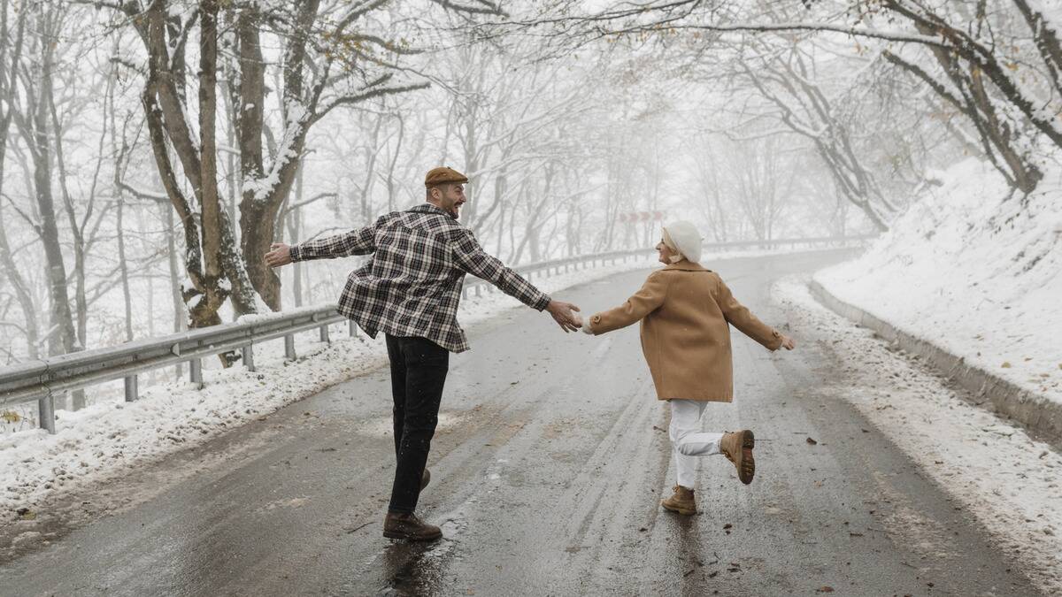 A couple smiling as they run together down a snowy winter street, arms out and looking at each other.