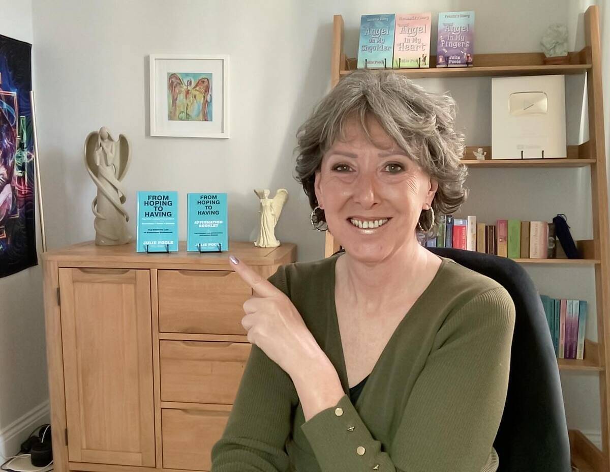 Poole at her desk, pointing toward the display of her own books behind her.