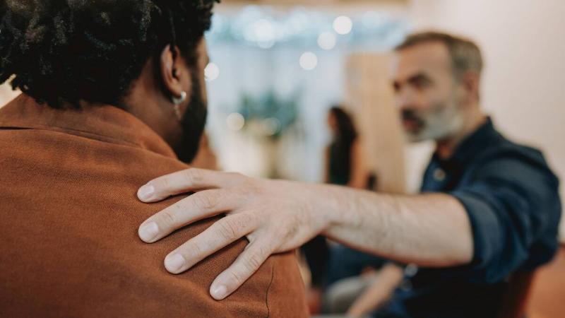 A man reaching over to another man, putting a comforting hand on his shoulder.