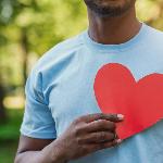 A man holding a paper cutout of a heart over his chest.