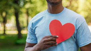 A man holding a paper cutout of a heart over his chest.