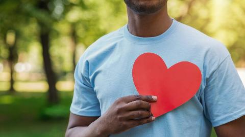 A man holding a paper cutout of a heart over his chest.