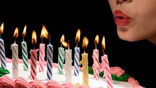 A close shot of a woman pursing her lips to blow out candles on a birthday cake.