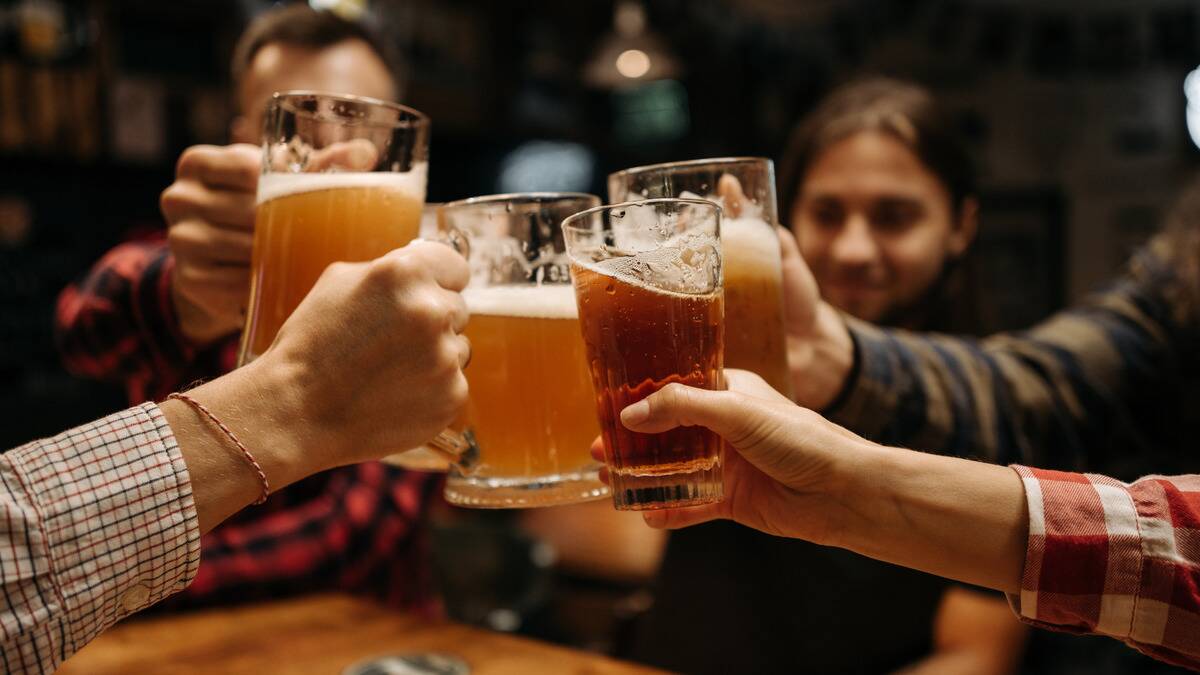 A group of friends at a bar 'cheersing' their various pints of beer together.