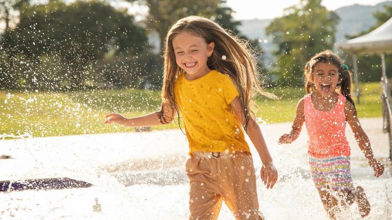 Two young girls playing in an outdoor splashpad, smiling as they run.