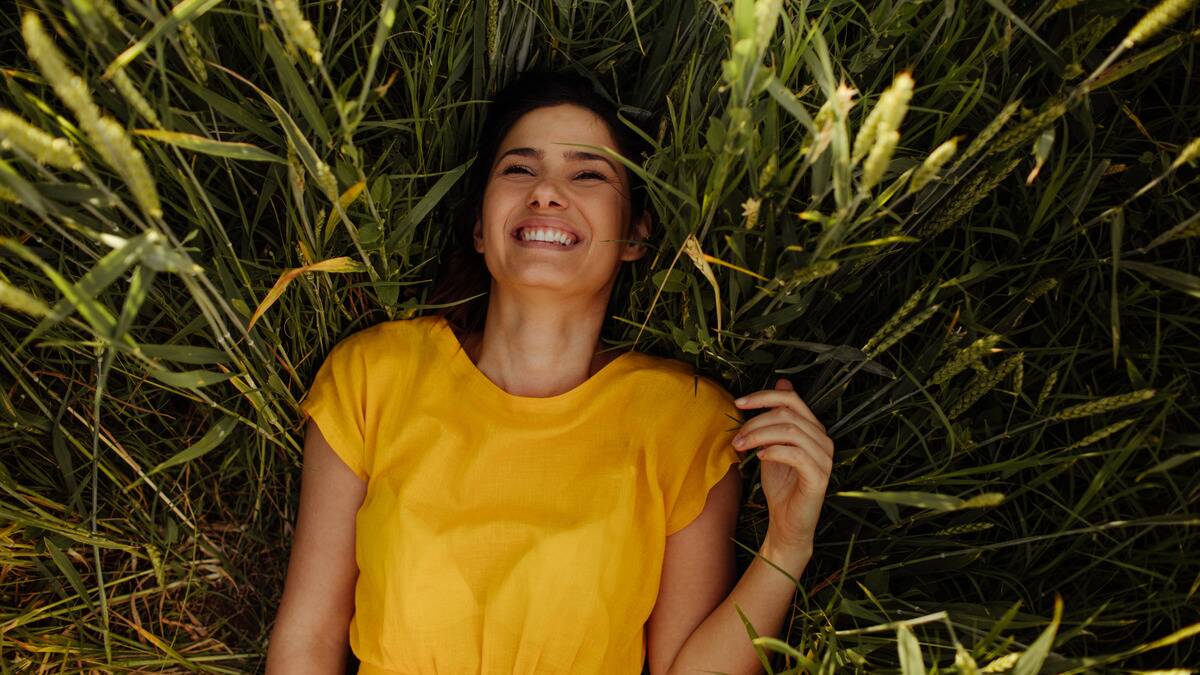 A woman laying in a patch of tall grass, smiling joyfully.