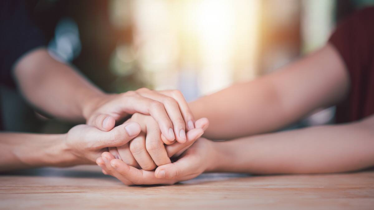 A close shot of someone holding another person's hands in their own, a comforting motion.