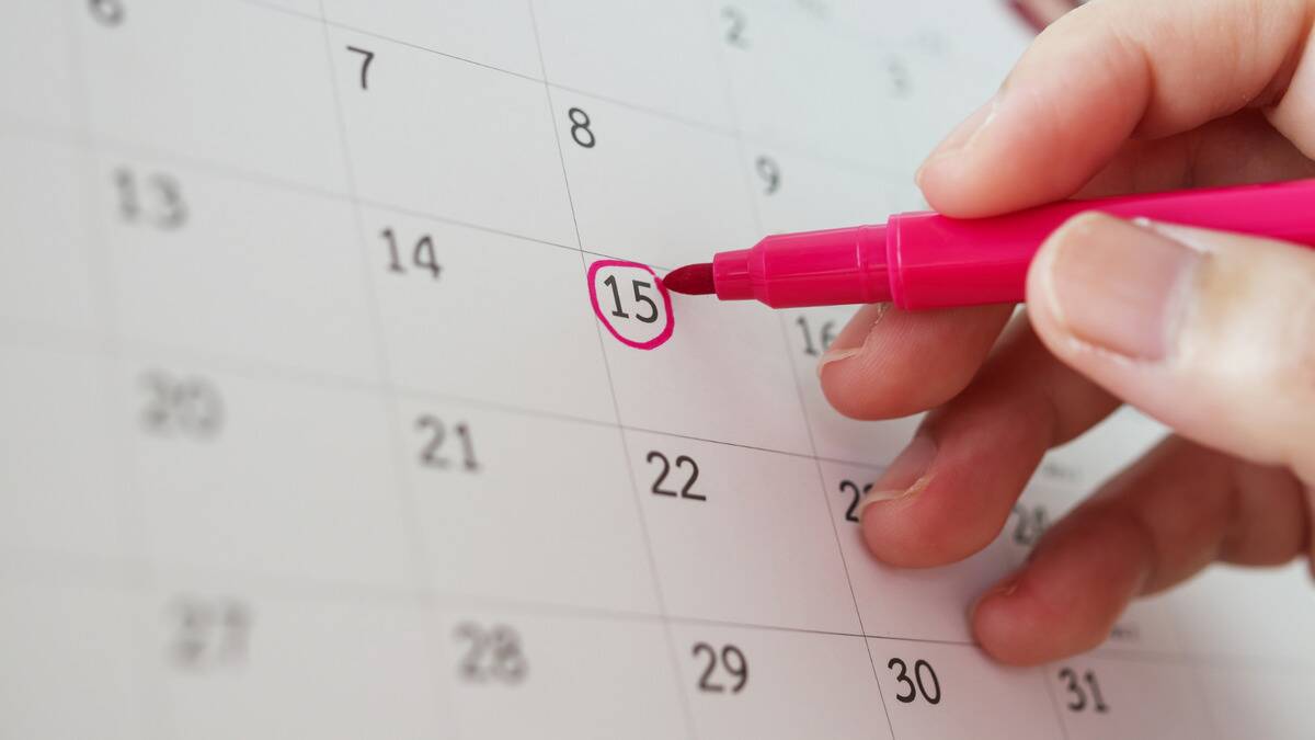 A close shot of someone circling the 15th on a monthly calendar with a pink marker.