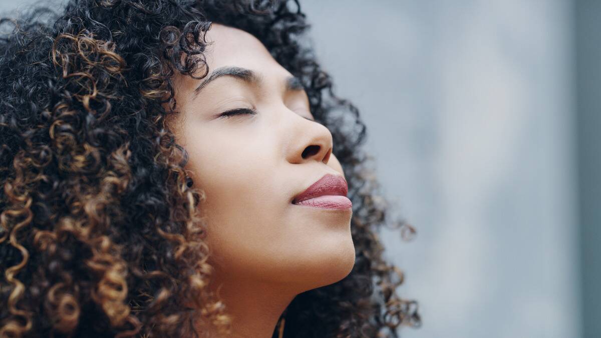 A close shot of a woman with her eyes closed, head tilted up slightly, smiling peacefully.