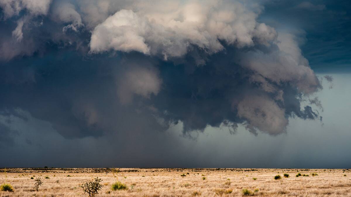 Dark storm clouds rolling over a plain, some rain seen falling in the distance.