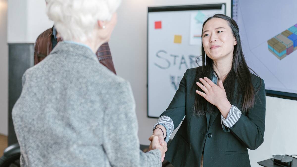 A woman shaking another woman's hand, looking grateful, one hand over her heart.