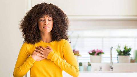 A woman standing with both of her hands over her heart, eyes closed peacefully.