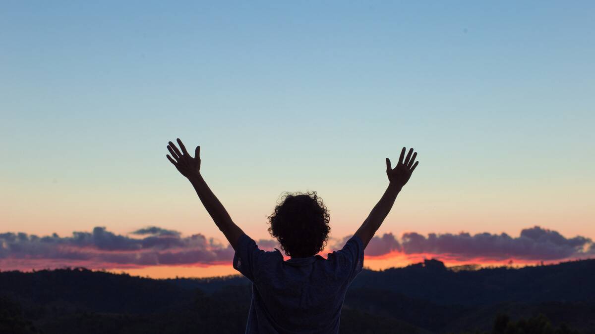 The silhouette of someone standing in front of a sunset horizon, arms outstretched into the air.