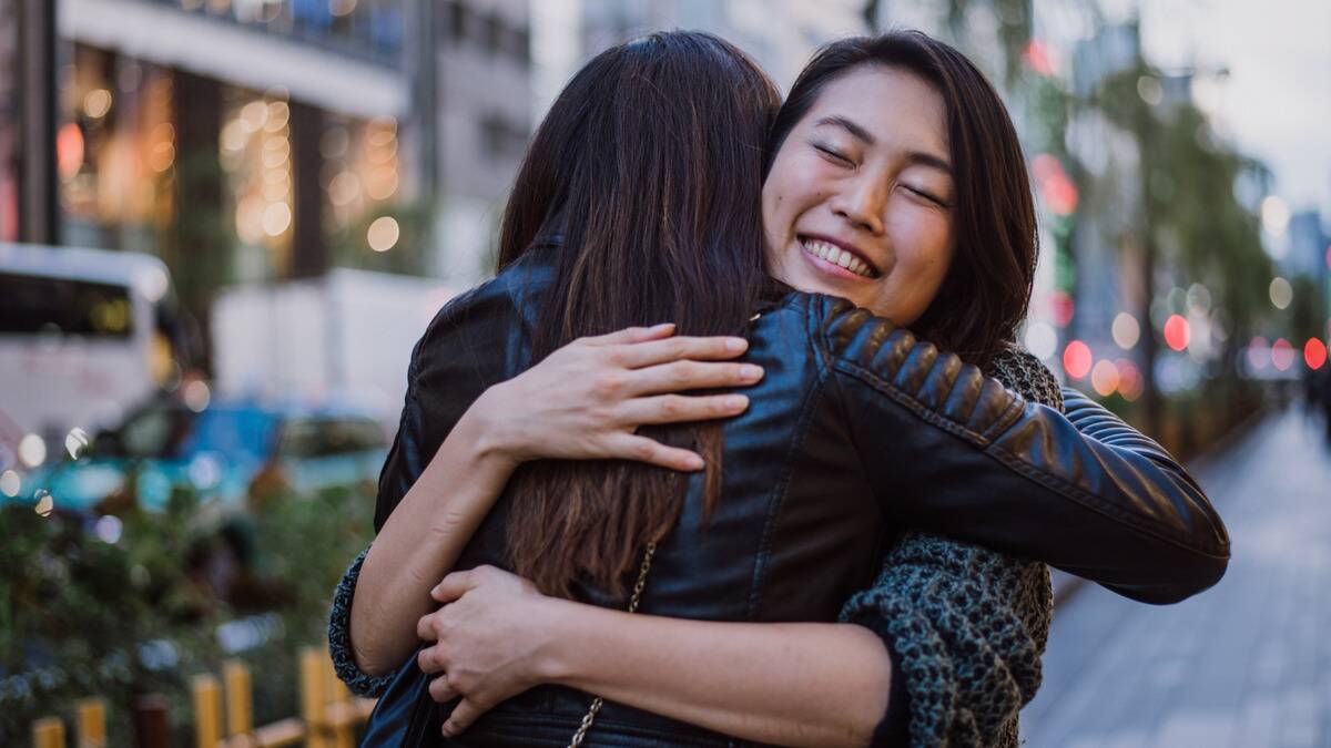 Two friends hugging outside, the friend whose face we can see smiling brightly with her eyes closed.