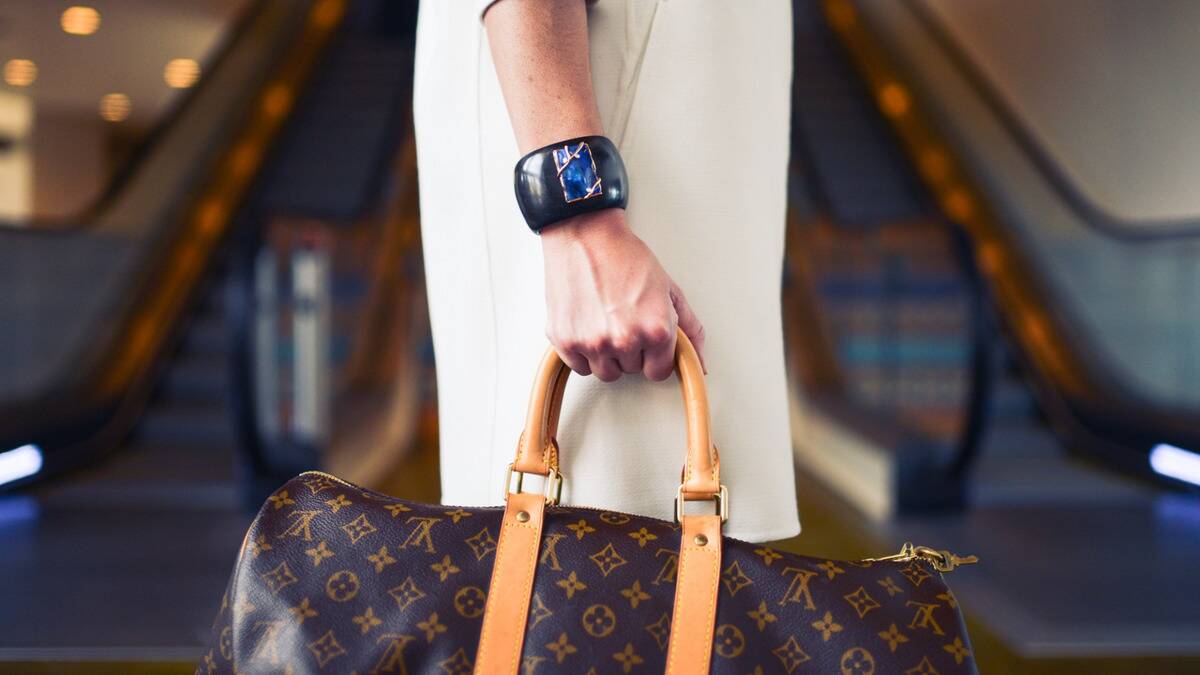 A close shot of a woman carrying a Louis Viton bag, wearing a chunky bracelet.