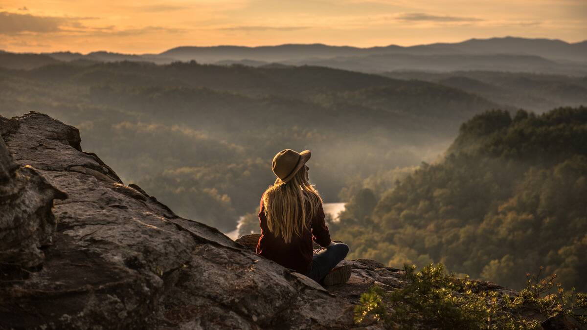 A woman sitting in a mountain range, looking out at the horizon.