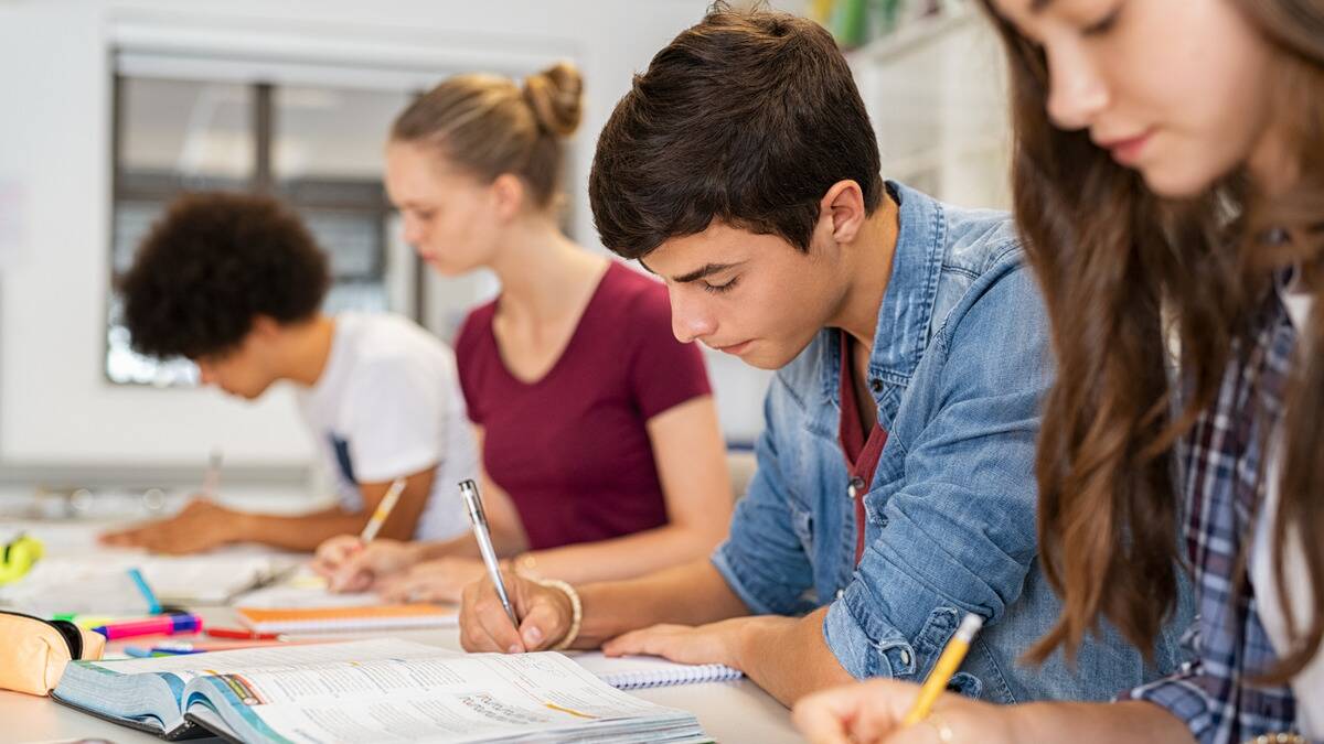 A man sitting at a desk among a row of students, all working on their schoolwork.