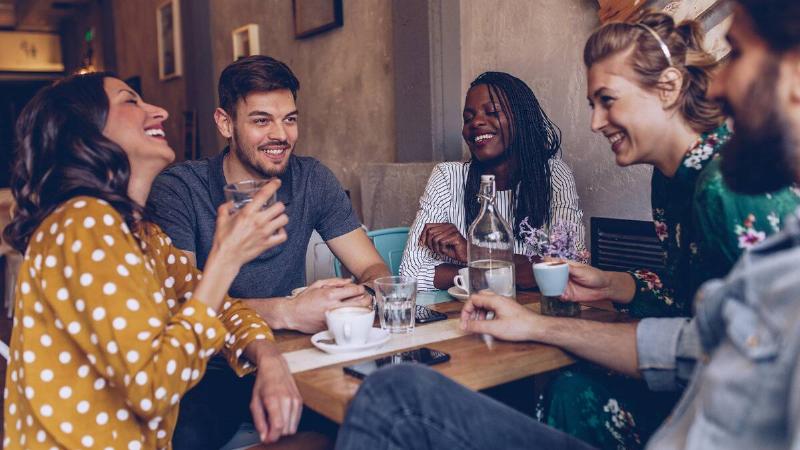 A group of friends sitting around a cafe table, laughing and smiling as they chat.