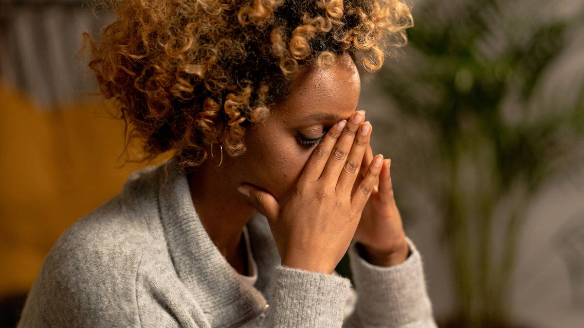 A woman sitting with her eyes closed, hands folded over the bridge of her nose, looking stressed.