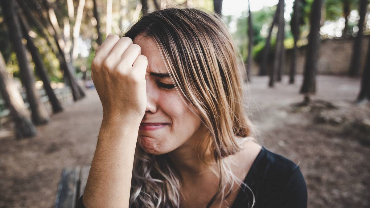 A close shot of a woman mid-crying, her balled up fist pressed against her nose.