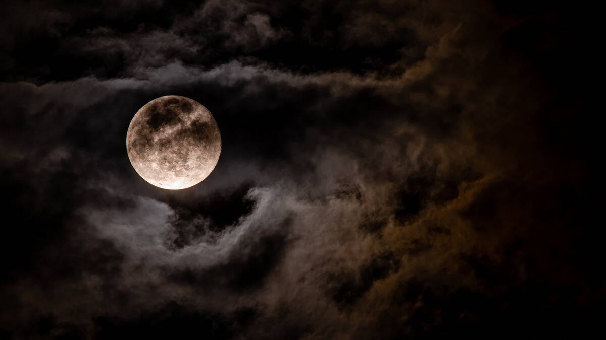 The full moon in a cloudy, dark sky.