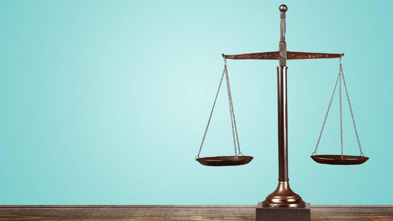 A set of justice scales on a table against a turquoise backdrop.