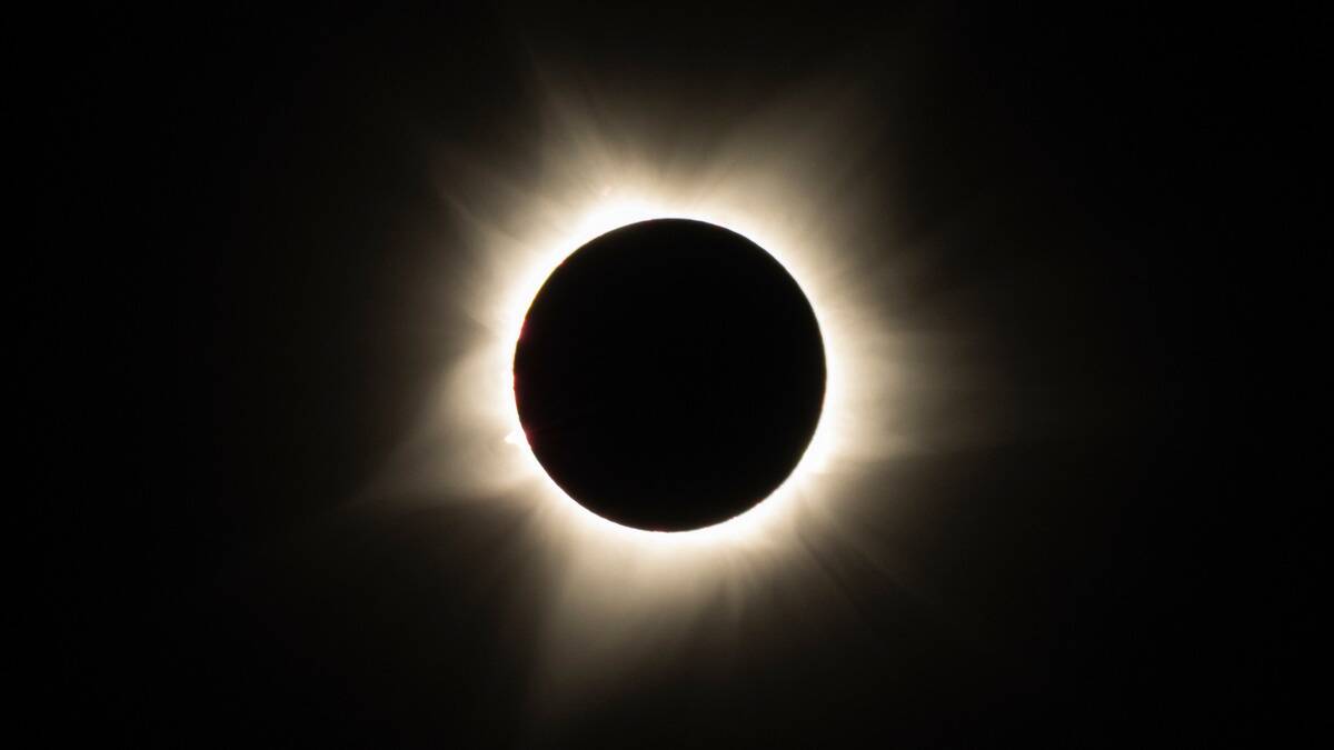 A solar eclipse, white feathered light leaking out from behind.