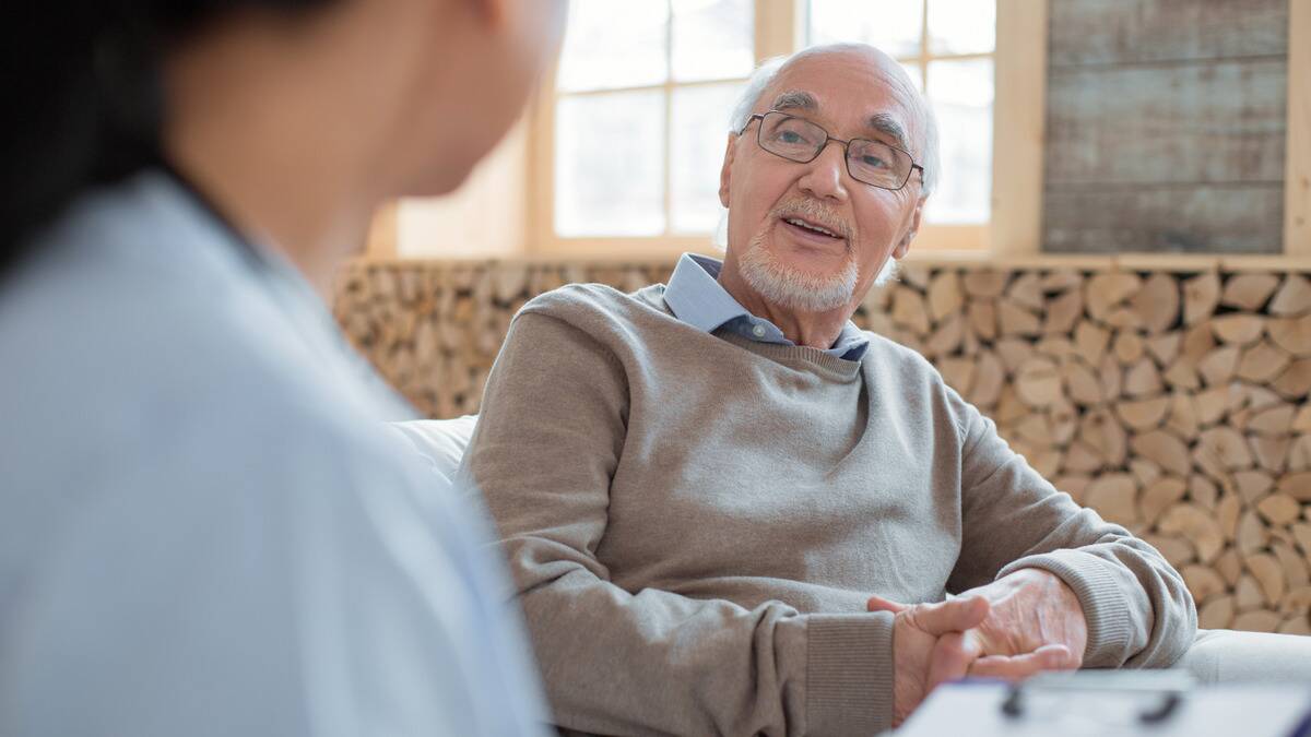 A senior man sitting and speaking to a younger woman whose shoulder we're looking over.