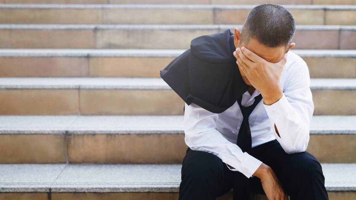 A man sitting on some outdoor city steps, elbows on his knees, his face in his hand and his jacket slung over his shoulder.