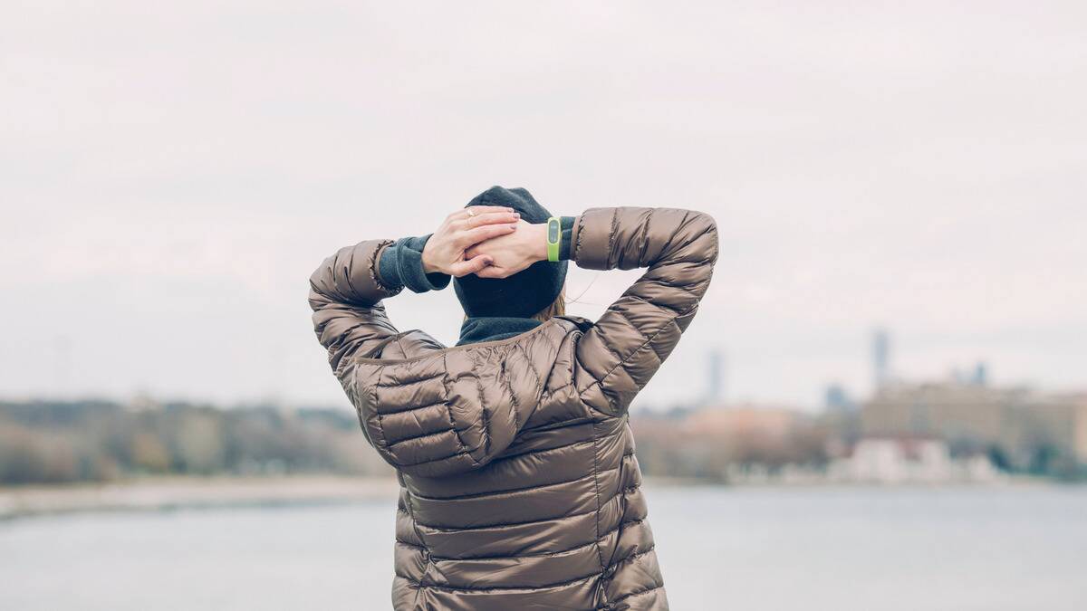 A woman standing outside in front of a small lake, hands together on top of her head as she looks out onto the horizon.