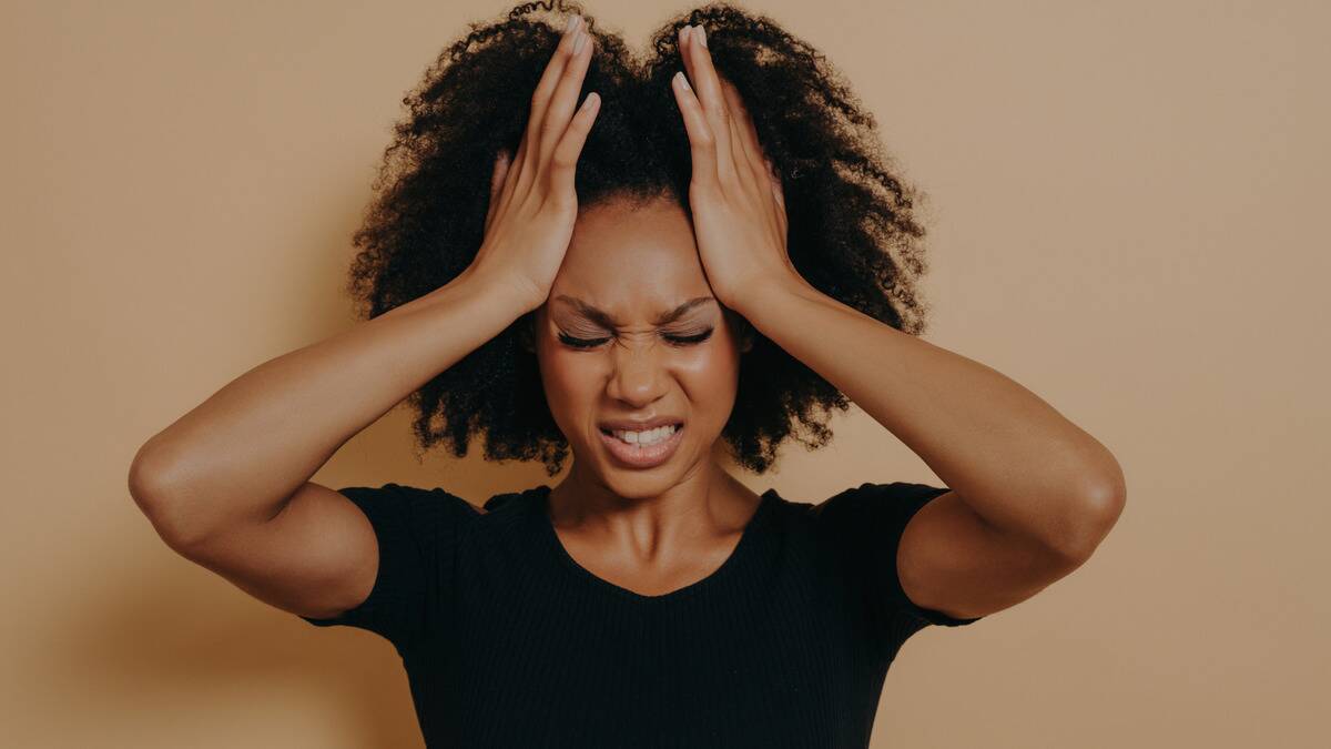 A woman with her face scrunched up in frustration and both hands on one of her temples.