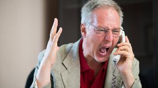 A man yelling angrily into a phone, his free hand gesturing as he shouts.