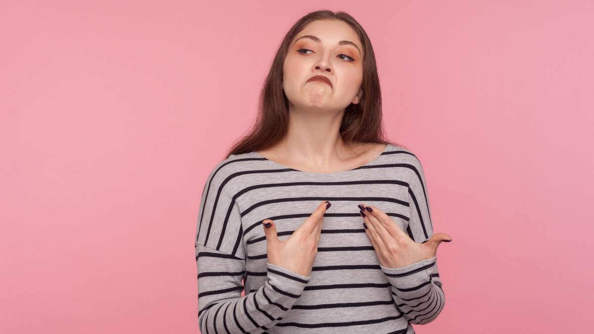 A woman against a pink background posing with a very cocky, smug expression.